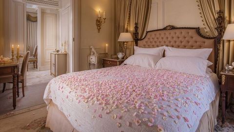 Romantic luxury bedroom suite featuring king-size bed strewn with pink rose petals