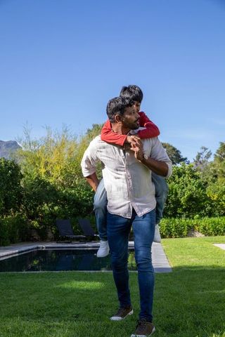 Father Giving Son Piggyback Ride Outdoors Near Pool