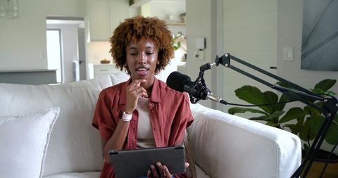 African american woman podcasting from living room with tablet and professional microphone