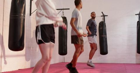 Group skipping rope cardio in boxing gym with heavy bags on pink mat