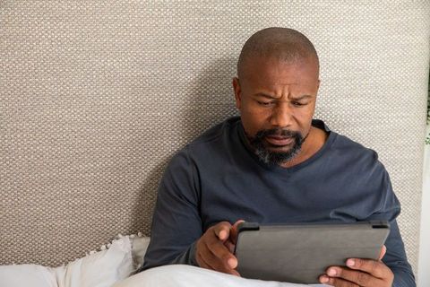 African american man reading tablet in cozy bed with textured headboard and neutral tones