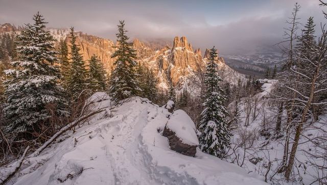 Snow-covered ridge trail leading to sunlit rock spires at alpenglow in winter mountains