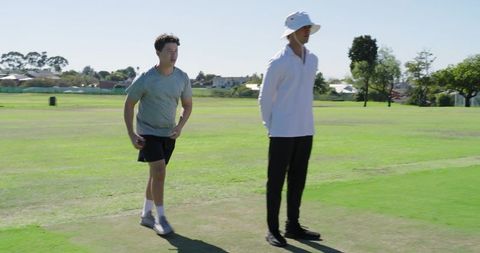 Youth cricket player sprinting past umpire on suburban grassy pitch during sunny practice
