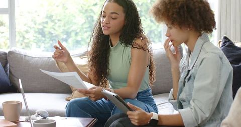 African American Women Reviewing Papers and Tablet on Sofa Collaborating on Finances