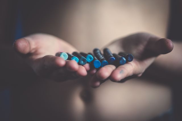 Close-up view of a child holding assorted blue crayons in open hands. Ideal for themes related to childhood, creativity, art, education, and children's activities. Can be used in blog posts, educational materials, or advertisements for art supplies.