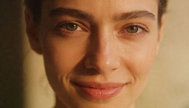 Close-up portrait woman with green-hazel eyes smiling warmly, natural skin texture
