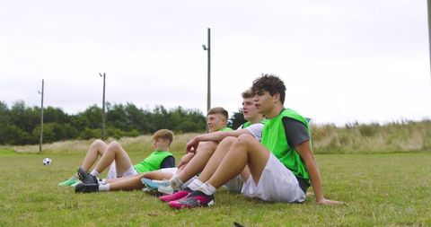Teenage soccer team resting on field in green training vests