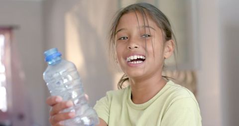 Smiling Biracial Girl Holding Plastic Bottle for Recycling at Home