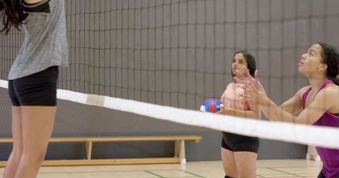 Young female athletes practicing volleyball on indoor court passing ball over net