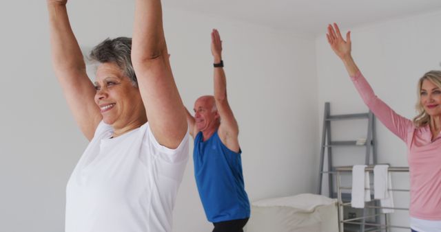 Seniors engaging in a group fitness class indoors, performing stretching exercises with smiles. Ideal for use in health and wellness campaigns, advertisements for senior fitness programs, chiropractic and physical therapy promotions, and editorial content about active lifestyles in retirement.