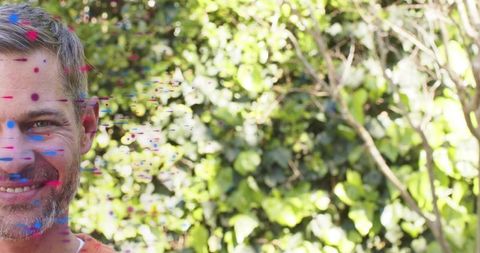 Smiling mature man posing in garden with colorful paint splashes and lush ivy backdrop