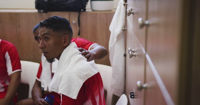 Athlete in red uniform sitting in locker room cooling down after an intense game. Perfect for sports, athleisure marketing, team bonding, and fitness-themed promotions.