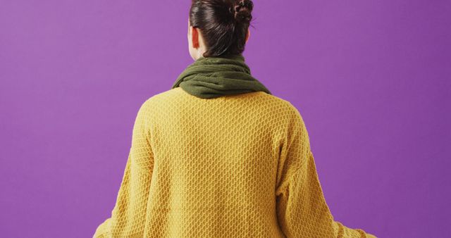 Person sitting cross-legged in a meditative pose wearing a yellow sweater and green scarf, viewed from behind. This can be used in wellness, health, or lifestyle content to promote relaxation, concentration, and mindfulness. Ideal for blogs, social media posts, or wellness programs focusing on peace and mental health.