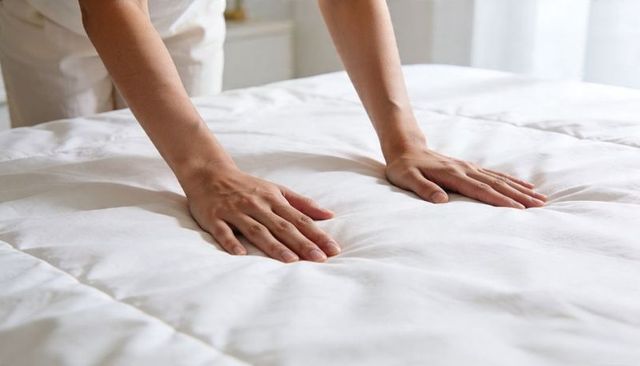 Hands pressing plush white comforter on bed testing softness and loft in sunlit room