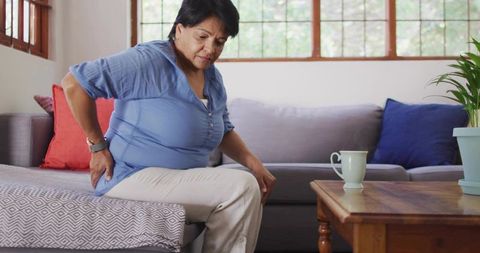 Senior Indian woman experiencing lower back pain while sitting on couch at home