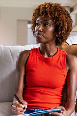 African american woman sitting on sofa holding tablet and stylus during thoughtful home planning