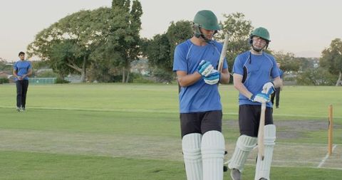 Diverse cricket teammates walking and planning strategy on green pitch wearing helmets