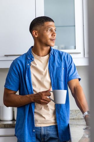 African-american man holding mug, gazing thoughtfully by modern kitchen countertop, calm