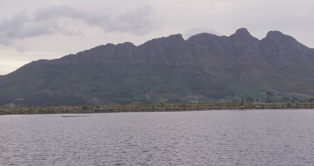 This stunning image depicts a serene mountain range seen from across a calm lake under an overcast sky. Ideal for use in travel brochures, nature magazines, and websites emphasizing outdoor adventure, tranquility, and natural beauty. Suitable as a background for presentations and blog posts promoting tourism, relaxation, and scenic views.