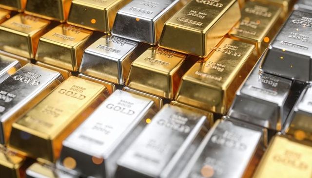Stacking gleaming gold and silver bullion bars with assay stamps on reflective surface