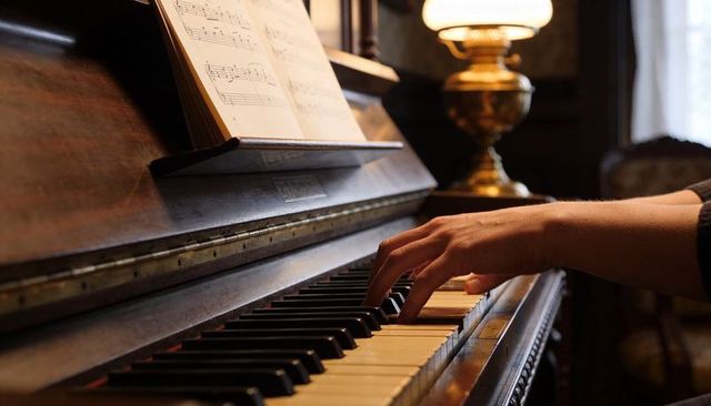 Hands playing vintage upright piano, sheet music on stand, warm lamp glow in parlor