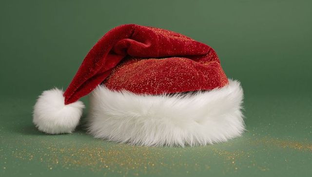 Resting red velvet Santa hat with white fur trim and gold glitter on green backdrop