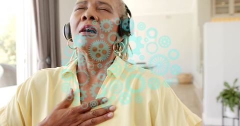 Senior woman listening with headphones holding chest turquoise gears overlay for mindfulness