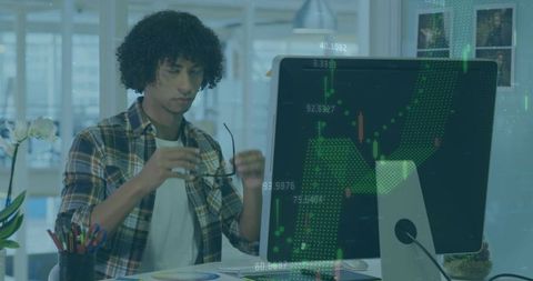 Young analyst holding glasses and focusing on desktop with financial candlestick charts