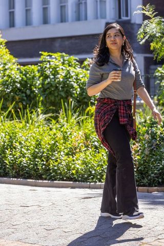 Young woman walking with takeaway coffee on sunny urban campus pathway