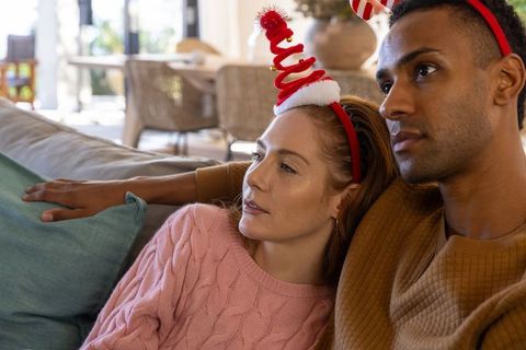 Diverse couple relaxing with festive headbands in living room