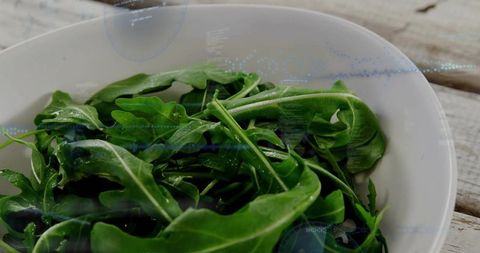 Fresh arugula leaves sitting in white ceramic bowl on rustic wood table