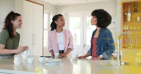 Friends Chatting Over Tea at Sunlit Modern Kitchen Island Pouring Tea and Smiling