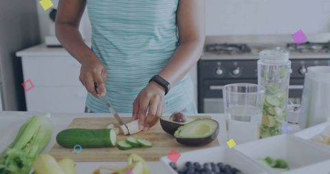 Preparing fresh cucumber and avocado for green smoothie, wearing fitness tracker