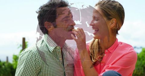 Couple sharing playful bite in sunny park, woman feeding man, laughter and romantic connection