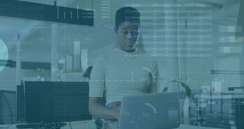 Standing professional analyzing data on laptop with HUD overlay in modern office
