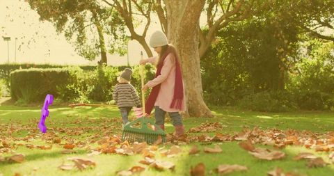 Sibling kids raking autumn leaves in park sister wearing pink coat brother walking playful