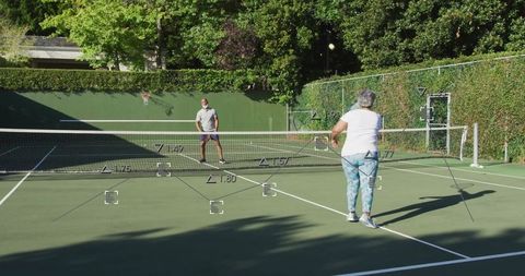 Senior Couple Playing Tennis on Outdoor Court in Bright Sunlight