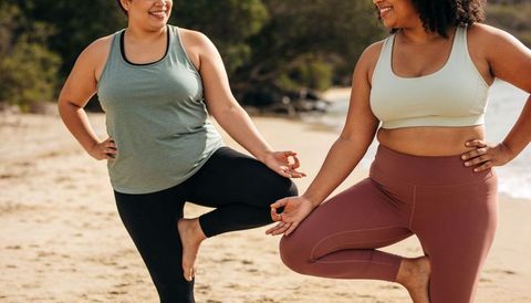 Plus-size women practicing yoga on beach balancing in tree pose for body-positive wellness
