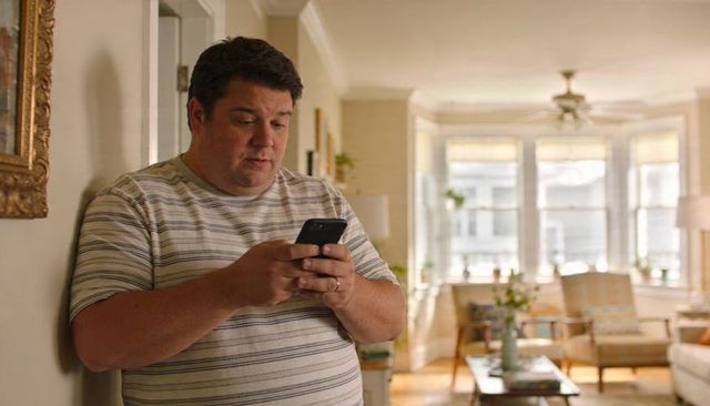 Standing adult man checking smartphone in bright home hallway with living room background