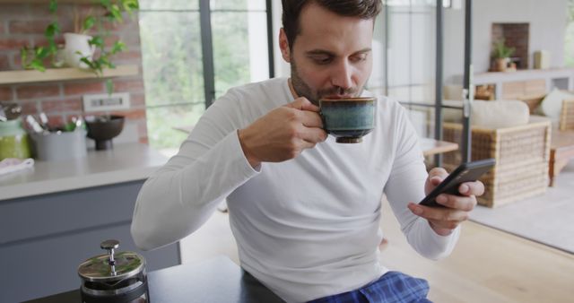 Young man in modern kitchen drinking coffee and checking smartphone - Download Free Stock Images Pikwizard.com