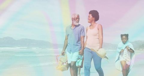 Multigenerational family walking on sunlit beach carrying picnic basket and straw hat