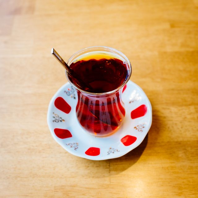 Traditional Turkish tea displayed in an ornate glass cup with a small saucer featuring red patterns, providing an authentic cultural touch. Commonly used for travel blogs, cultural articles, coffee shops, and culinary magazines to depict Turkish lifestyle or tea culture.