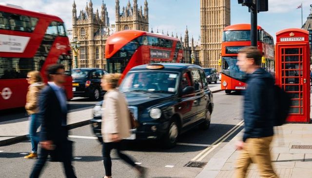 Motion-blurred london commuters crossing by elizabeth tower with black taxi and red buses