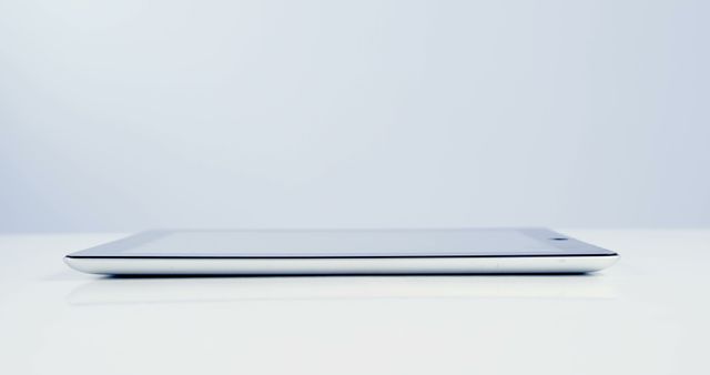 A modern tablet lies on a white surface, showcasing its slim profile and minimalist design, with copy space. Its sleek appearance emphasizes the advancements in portable technology and digital connectivity.