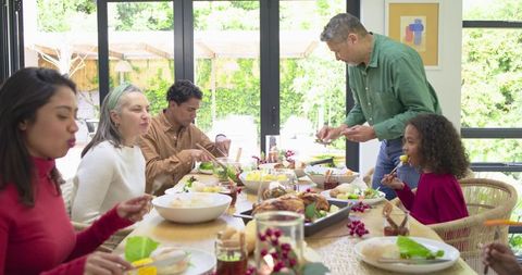 Multigenerational Family Sharing Festive Meal Around Sunlit Dining Table With Roasted Bird
