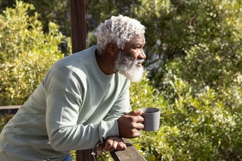 Senior african-american man leaning on balcony railing holding coffee mug enjoying sunrise calm