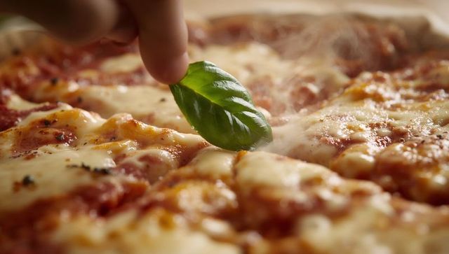 Hands adding fresh basil leaf to steaming margherita pizza with melted mozzarella