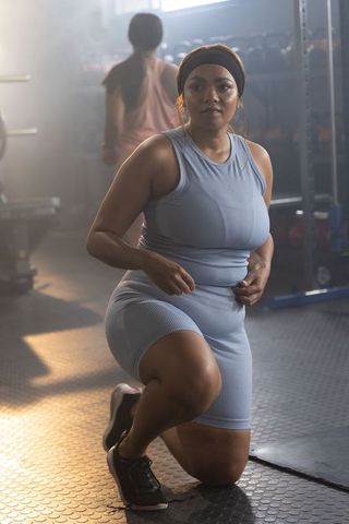 Kneeling woman preparing for intense gym workout in light blue activewear