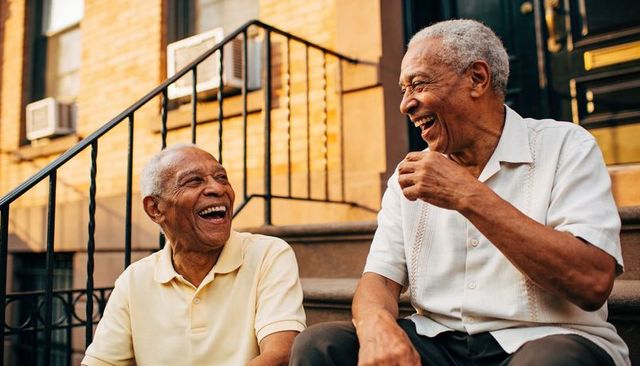 Two senior men laughing on brownstone stoop, chatting and sharing urban neighborhood joy