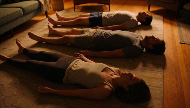 Three adults practicing guided relaxation on living room rug at home during warm evening